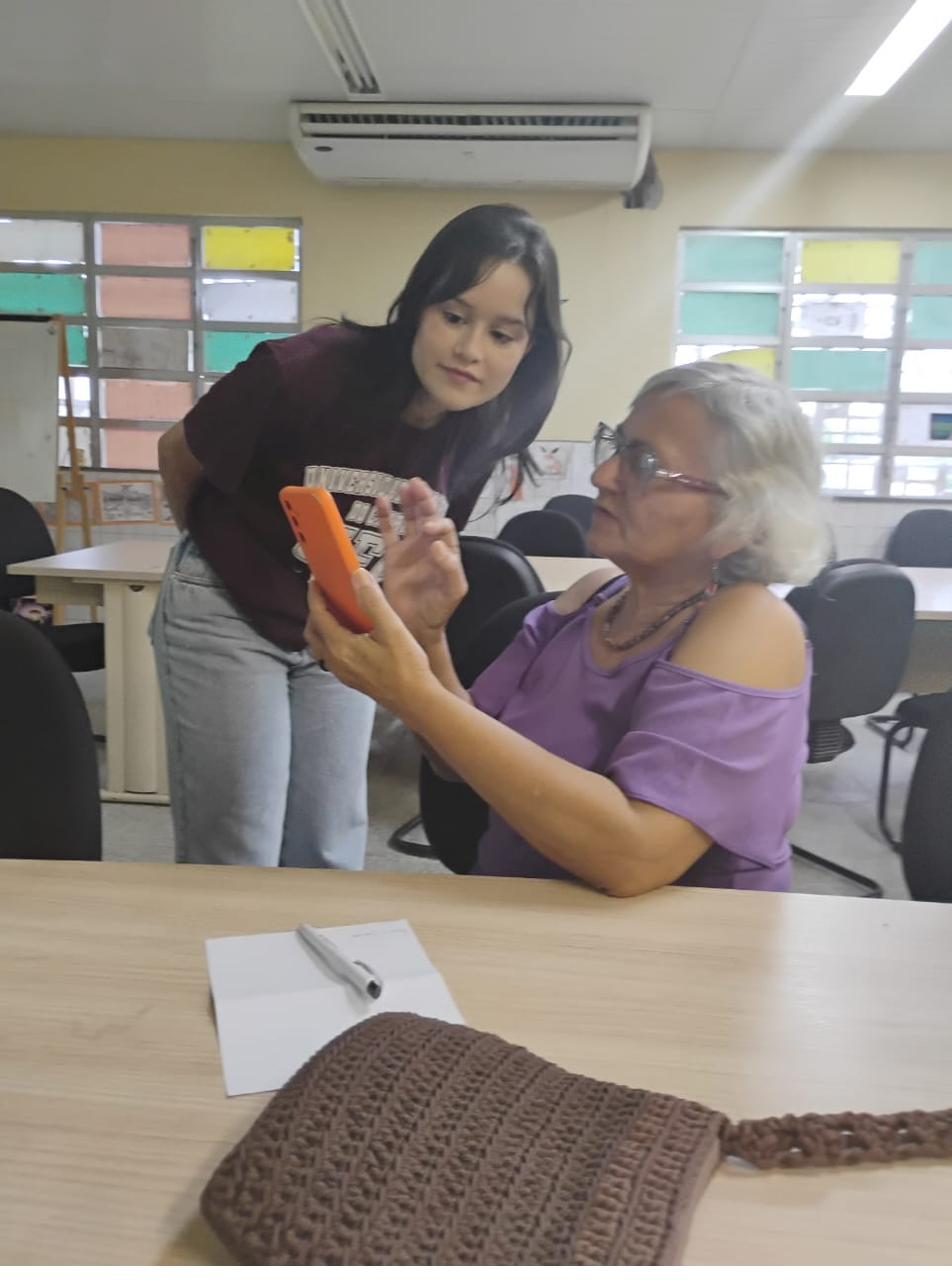 Cybele, voluntária do projeto, ao lado de uma participante observando o celular.