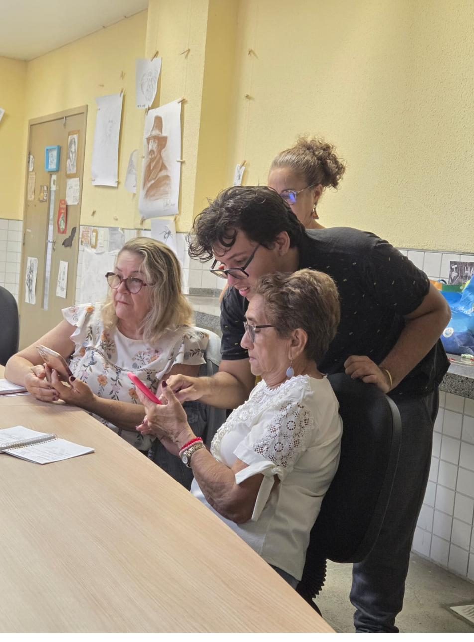Voluntários auxiliam participantes com seus celulares em mesa de trabalho.