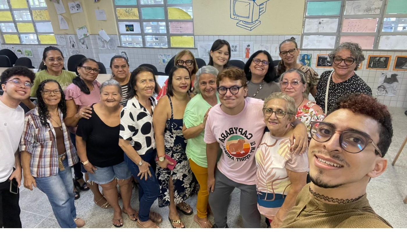 Grupo grande de participantes e voluntários reunidos na sala de oficinas, sorrindo para a foto.