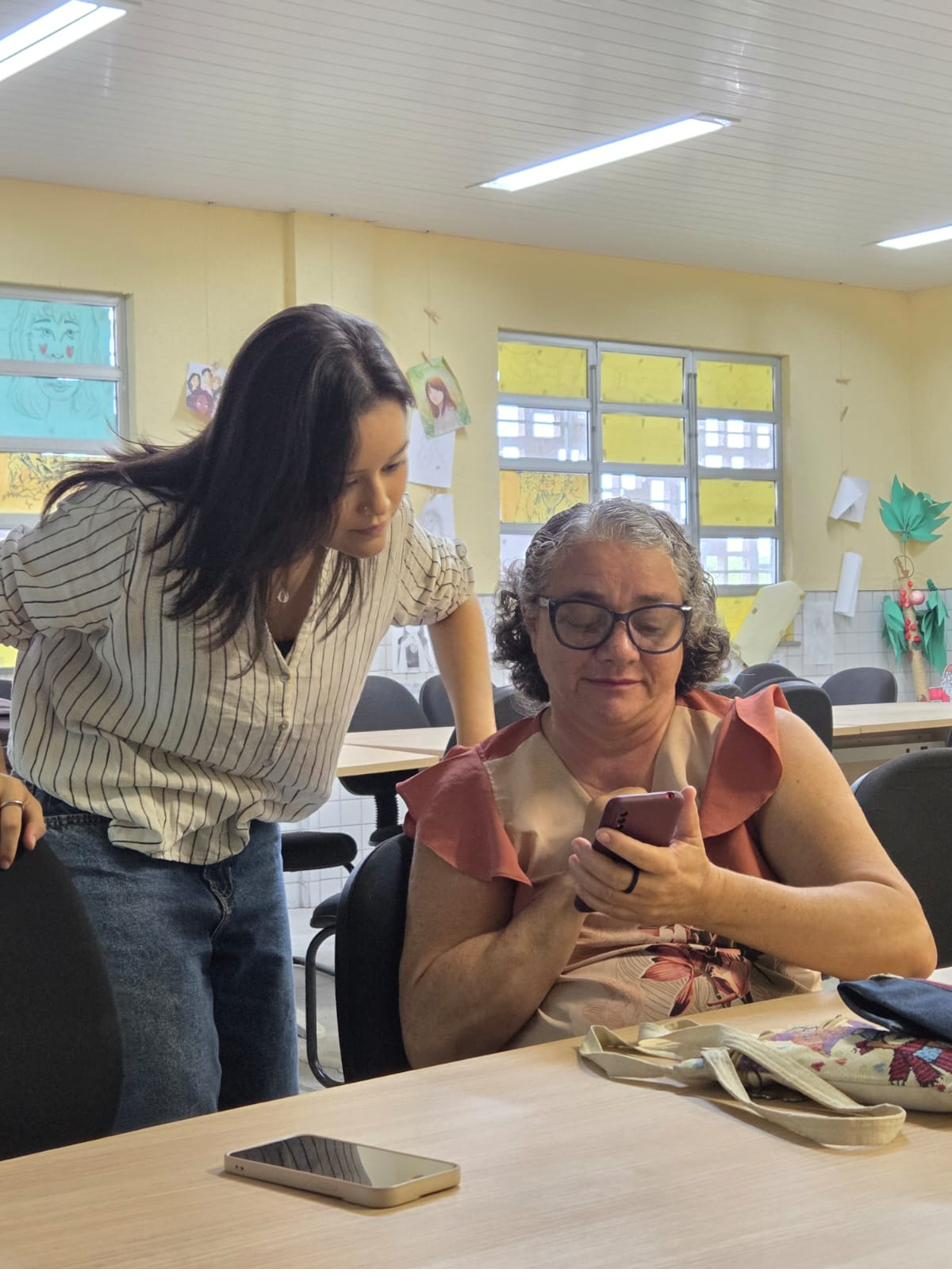 Voluntária do projeto ajuda uma participante a usar o celular durante uma oficina.