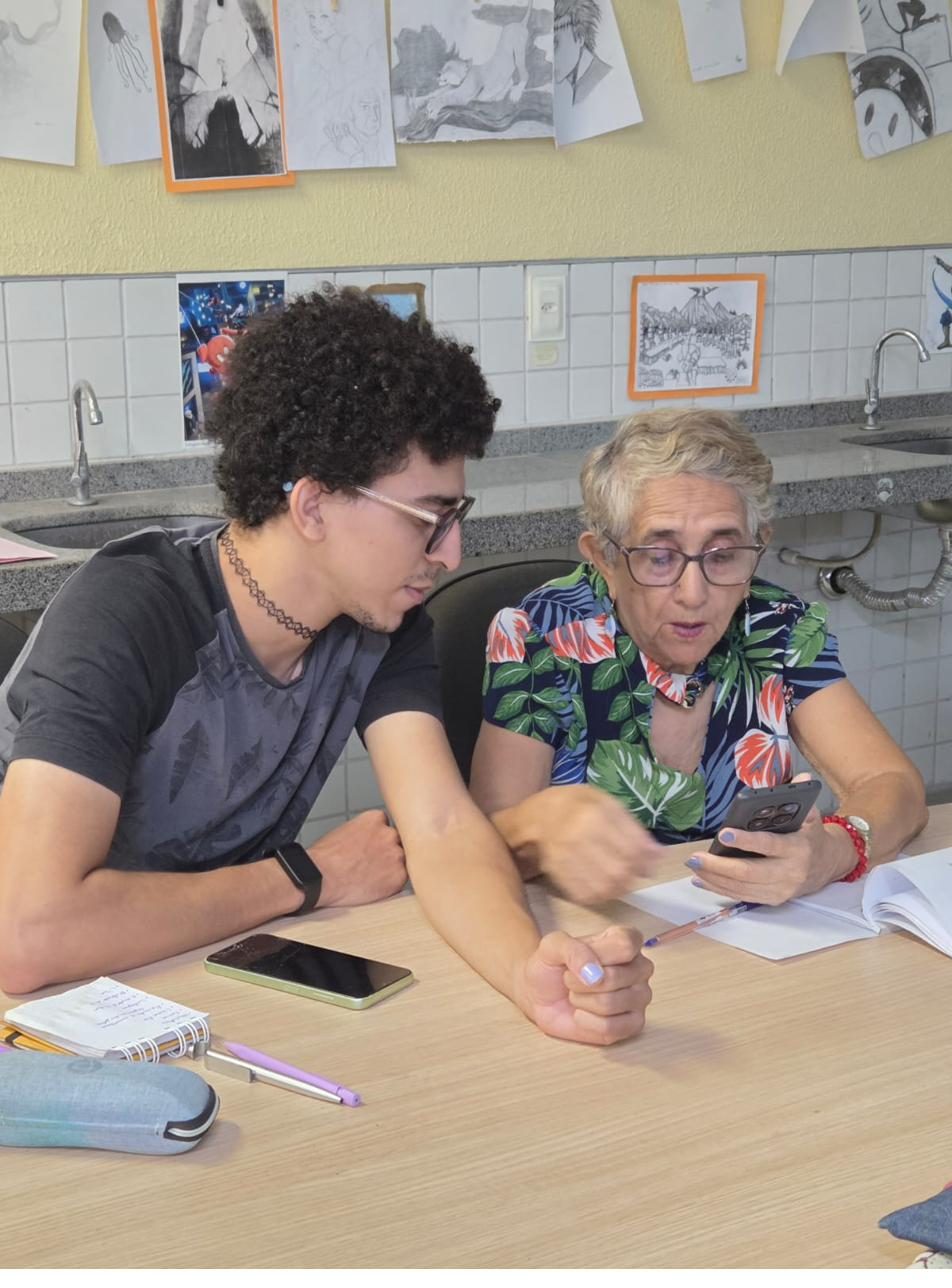 Voluntário mostra algo no celular para uma participante, lado a lado.
